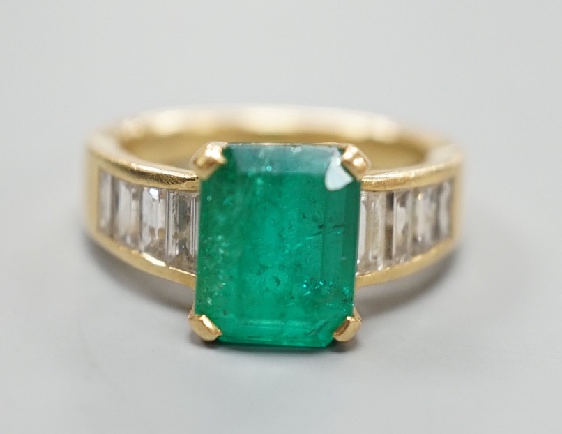 A modern yellow metal and single stone emerald set dress ring, with graduated baguette cut diamond set shoulders, size M/N, gross weight 7.3 grams.